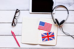 планшет, наушники, очки, ручка, тетрадь с лежащими на ней миниатюрными флагами Великобритании и США