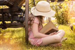 девочка с книгой руках и шляпке сидит у колеса телеги