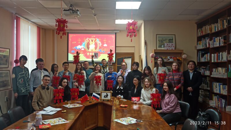 Китайцы и русские с красными фонариками в руках на фоне баннера с зайцем-символом года