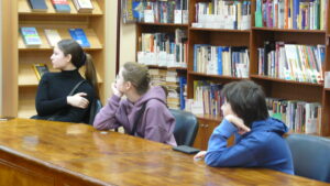 Трое подростков за большим столом на фоне стеллажей с книгами