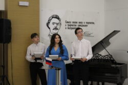Два молодых человека и девушка с микрофонами около рояля