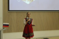 Девушка в красном сарафане с микрофоном перед экраном