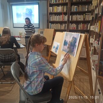 девочка сидит за мольбертом и рисует картину