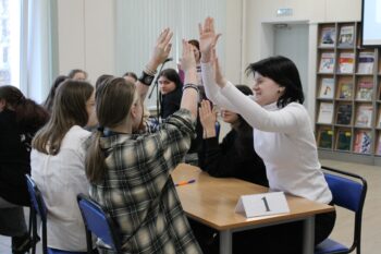 Подростки сидят за столом и выполняют упражнения для рук
